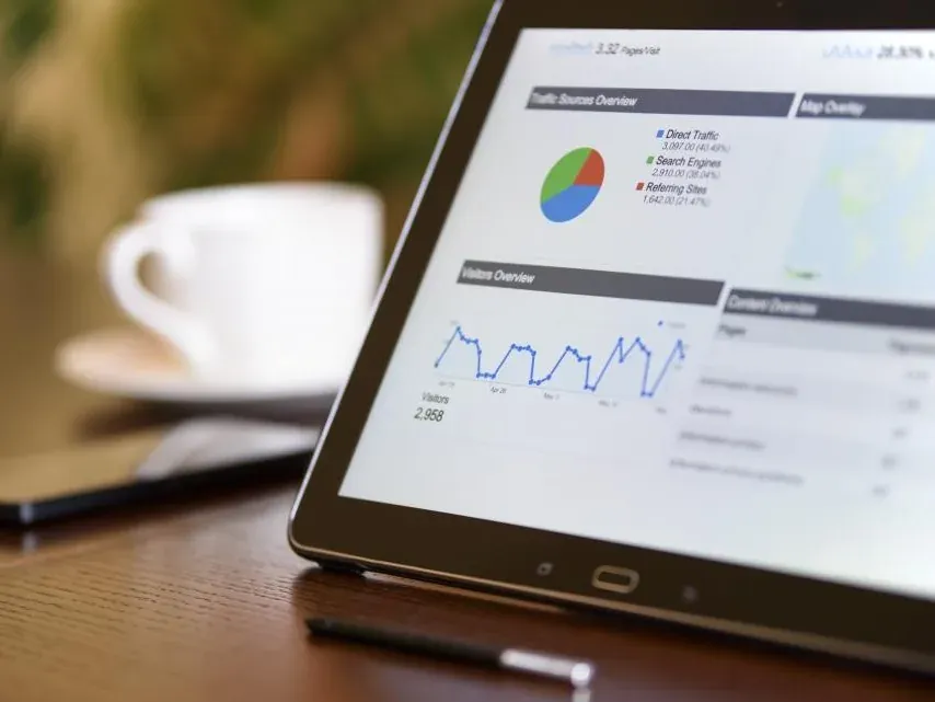 A tablet on a desk showing a marketing analytics dashboard with charts and a coffee cup alongside