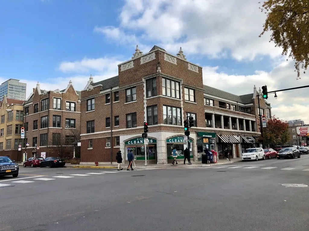 A brick corner building with ground-floor shops at a Chicago neighborhood intersection