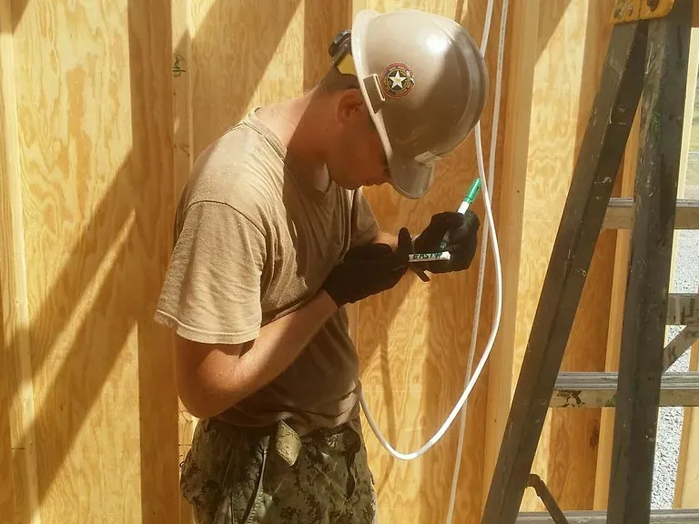 A carpenter in a hard hat working on timber wall framing inside a house under construction