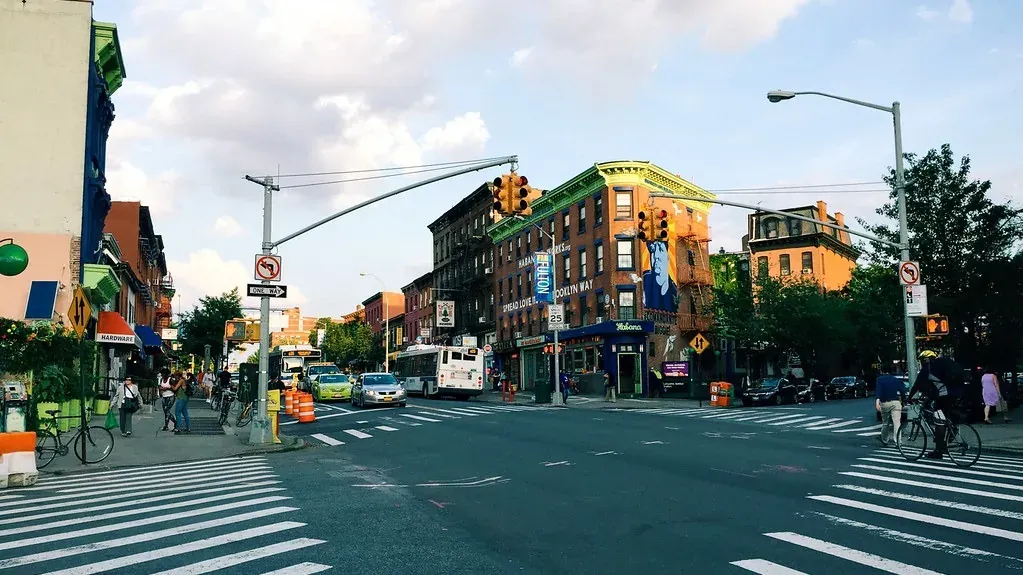 A wide neighborhood crossroads with painted crosswalks, traffic signals and low shopfronts