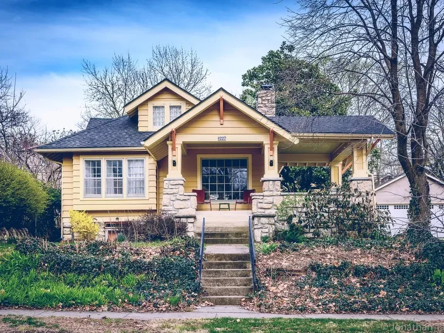 A timber-clad suburban craftsman house with a covered porch and mature front garden
