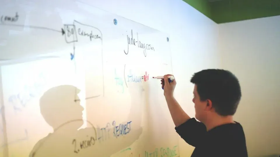 Someone drawing a process diagram in marker across a large office whiteboard